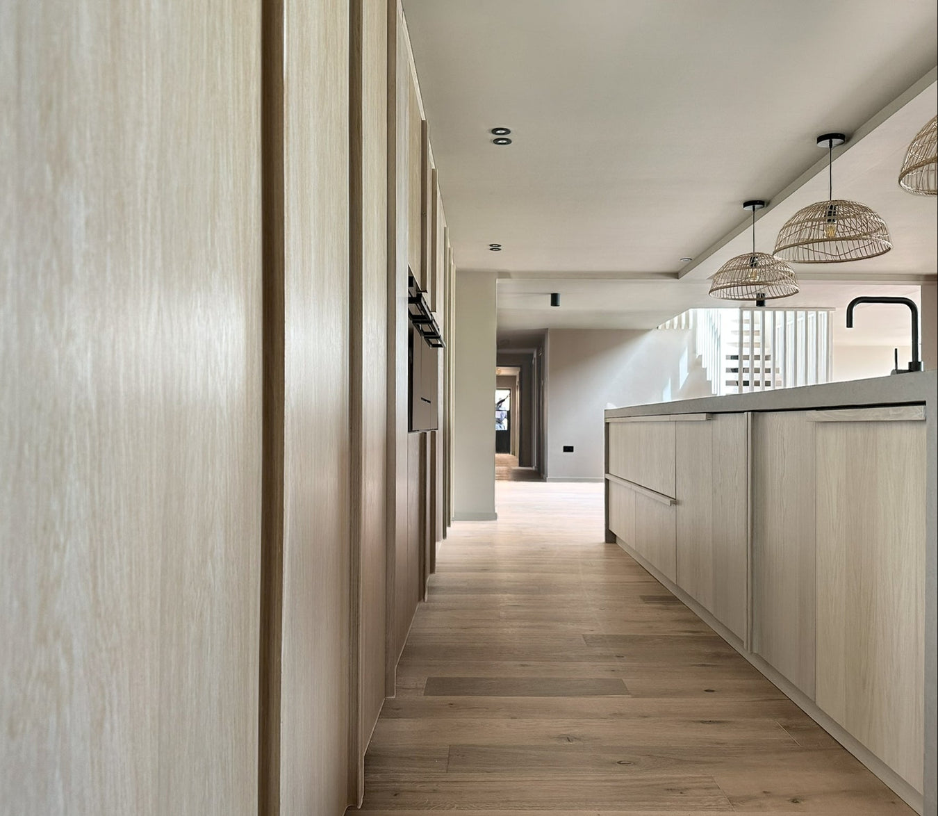 Modern kitchen with whitewashed oak cabinets and a view into another room.