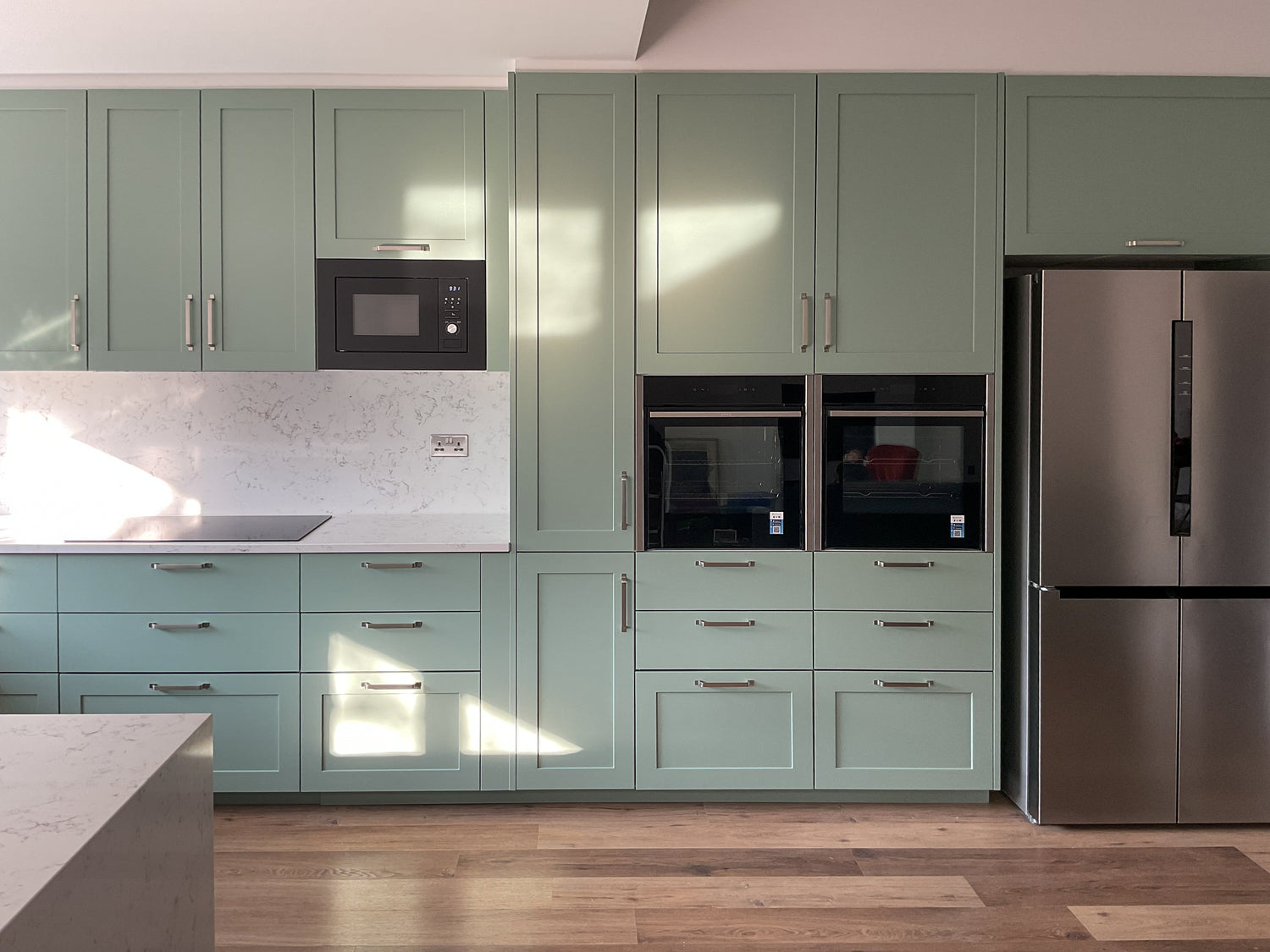Modern kitchen with green cabinets, stainless steel appliances, and wooden flooring.