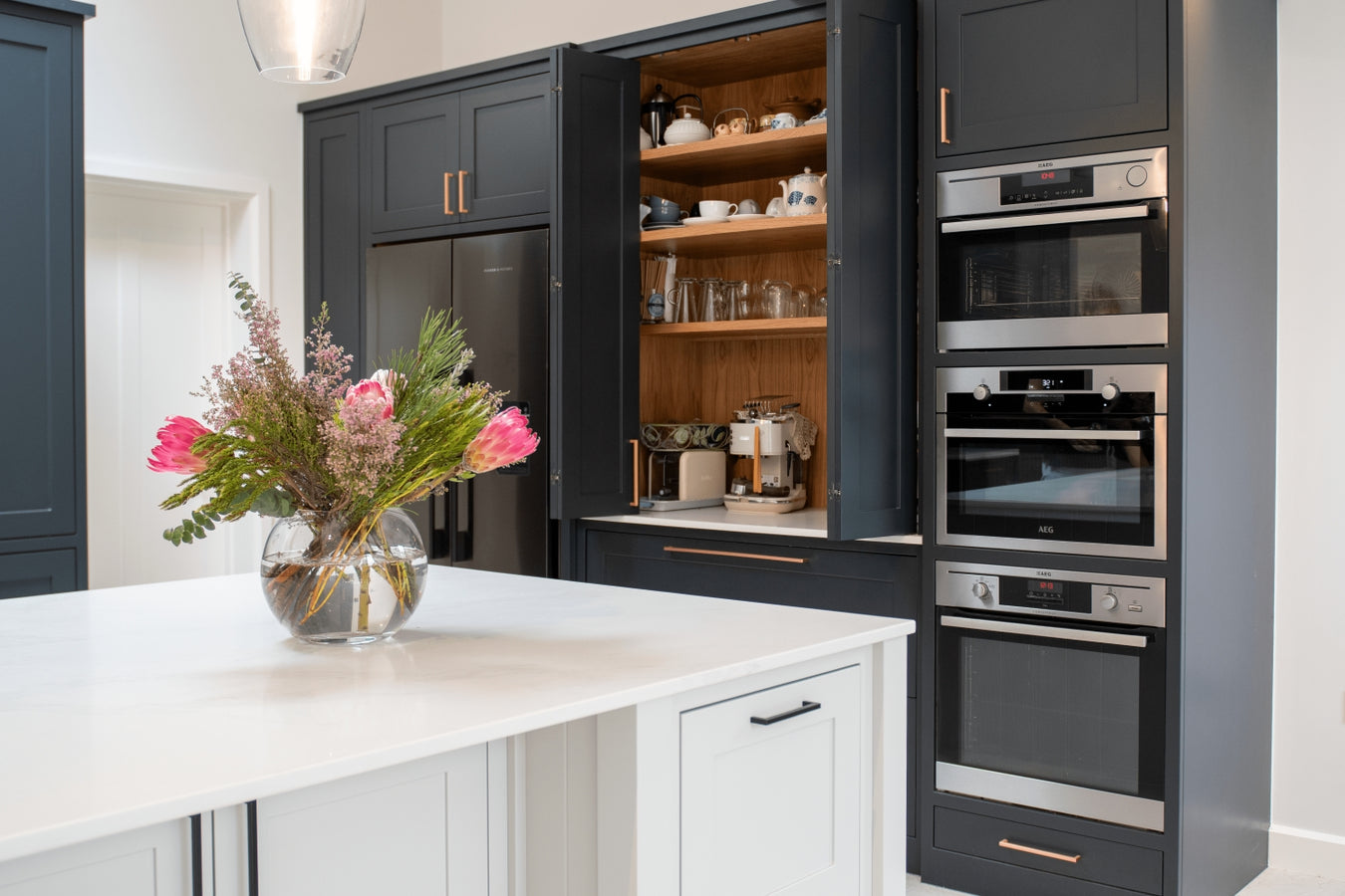 Inframe shaker kitchen cabinets, white quartz worktop, and a vase of flowers.