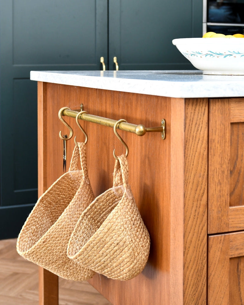 Oak kitchen island with wicker baskets hanging on a hook, dark cabinets in the background.