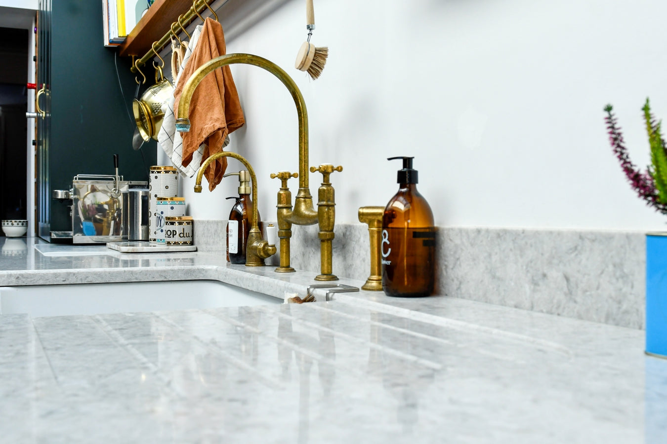 Modern kitchen sink area with brass tap and various bottles on a quartz worktop
