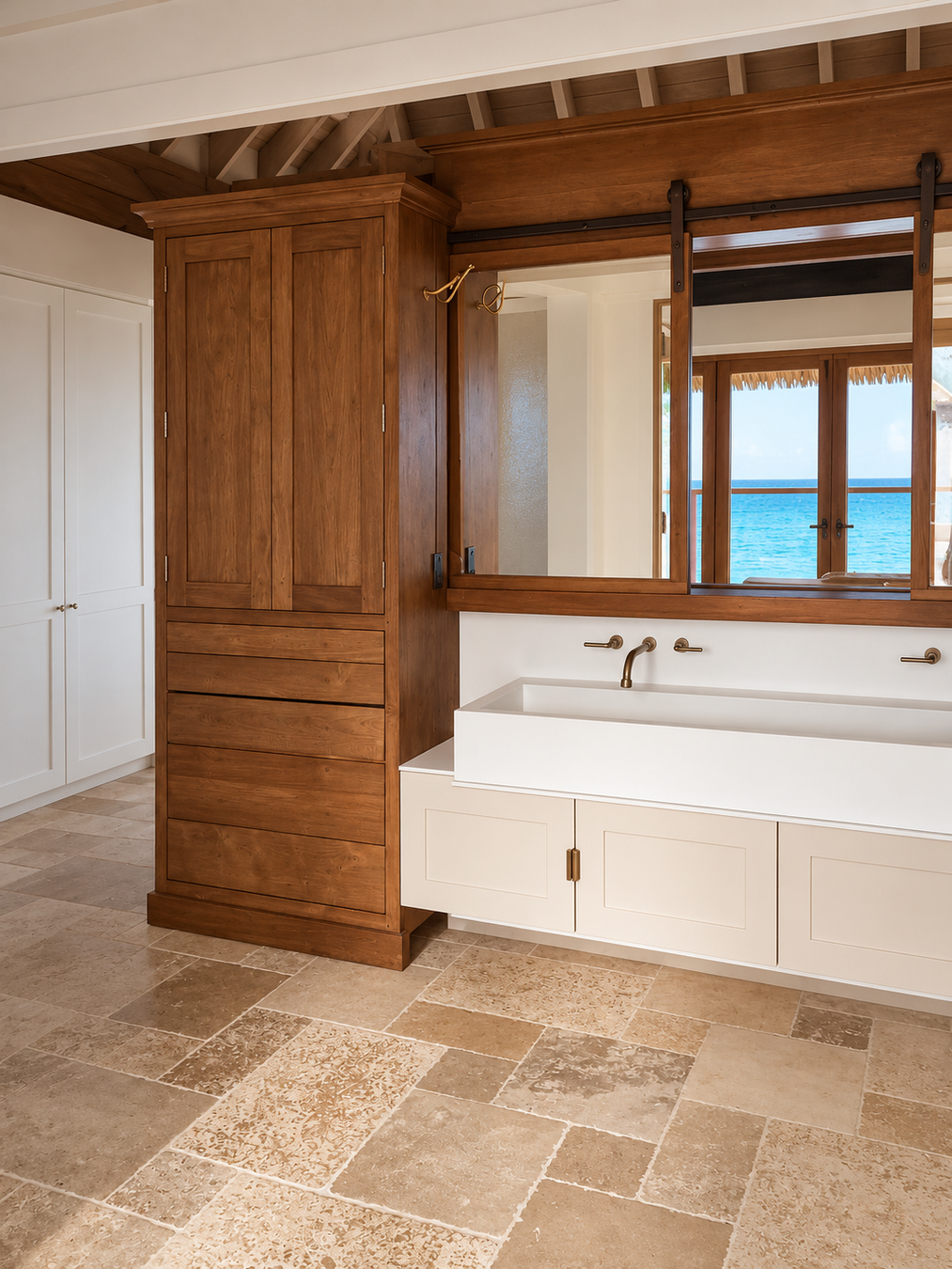 A luxury bathroom interior featuring a double-sink vanity with a white ceramic basin, a tall wooden cabinet, and a large mirror above. The room is styled with warm wood paneling, beige stone tile flooring, and an ocean view visible in the mirror reflection.